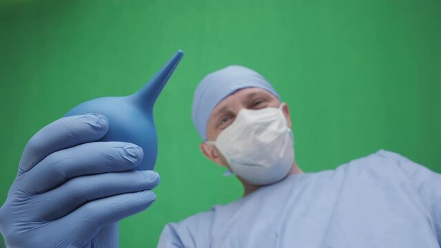 A physician with an enema. A doctor with an enema in his hands stands above the patient. First-person view, green screen background. Doctors face with an enema in front of a patient