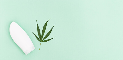 Cannabis beauty products that contain natural ingredients of plant origin. Jar of hemp cream and green leaf ob green paper background with copy space. Top view.