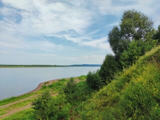 Fototapeta na wymiar green hillside near the river bank against a blue sky with clouds