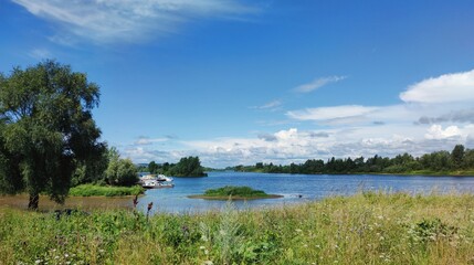 green river bank on the background of blue sky with beautiful clouds on a sunny day