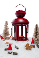 Red Christmas lantern on snow with pine cones, small cones, leaves, golden christmas trees, small golden baubles with santa hats in front of a white background, copy space