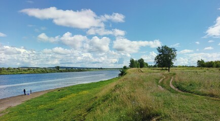 green river bank on a sunny day on a background of blue sky with clouds