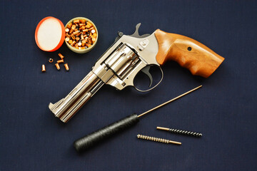 A revolver gun laying on a dark background with cleaning kit, bullets, brushes