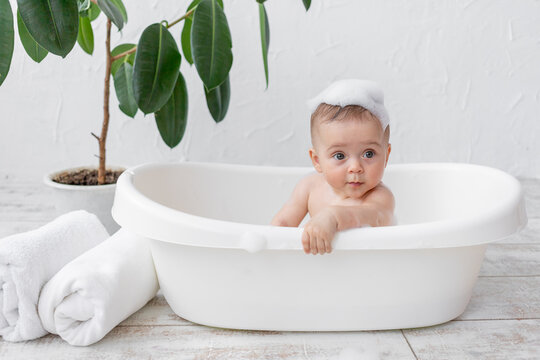 A small child boy 8 months old bathes in a bath with foam and soap bubbles, place for text
