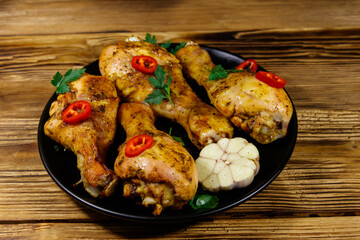 Roasted chicken drumsticks with spices in a black plate on a wooden table