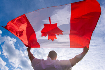 Man holding The National Flag of Canada against blue sky