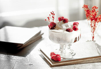 bowl with white ice cream, red berry jam and fresh raspberries on a light table in the backlight