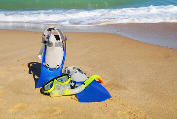 Obraz premium flippers and mask for swimming on the sand against the background of the sea and clear sky