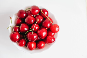 Fresh juicy red cherries in a white plate on the white wooden background. Top view. Copy, empty space for text