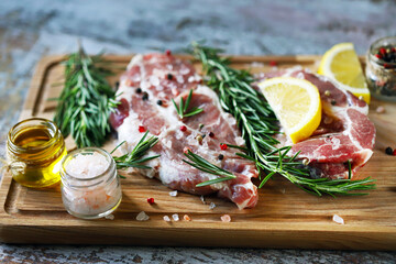 Selective focus. Raw meat with rosemary and spices on a wooden board. Raw pork steaks.