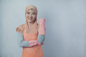 Fototapeta premium Young muslim woman housewife with pink rubber gloves in apron on grey background