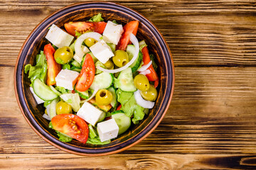 Ceramic plate with greek salad on wooden table. Top view