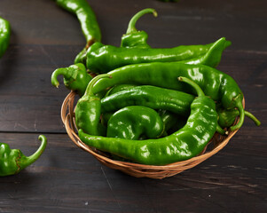green hot pepper pods in a round wicker basket on a brown wooden table