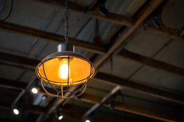 A retro style lighting lamp with warming light color shade. Photo with blurred background of metal ceiling structure building. Electrical object equipment.