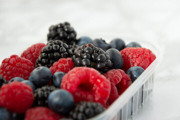 Berries in plastic tub on marble background