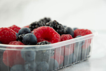 Berries in plastic tub on marble background