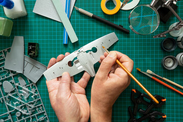 Overhead View Of Man Building Scale Model Aeroplane From Kit On Cutting BoardWith Tools And...