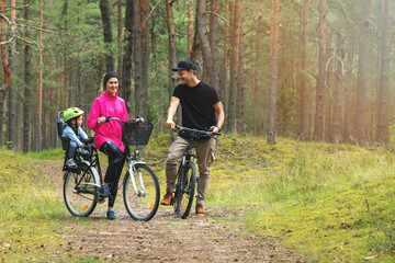 Fototapeta na wymiar young family cycling on forest trail with kid in bike child seat. active sports outdoor recreation