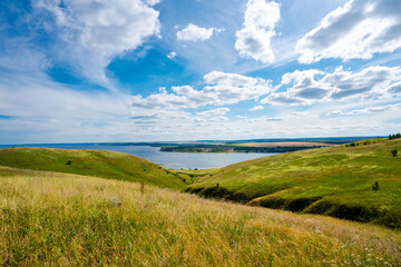 Fototapeta na wymiar Panorama of the Russian picturesque landscape with hills and flower fields and blue sky with clouds on the background of the sea