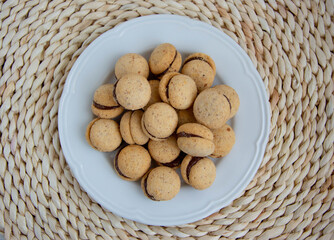 Baci di dama, lady kisses, on white plate Italian biscuits whit chocolate, background round wooden tablecloth