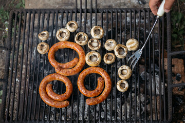 Mushrooms and sausages on grill in nature.