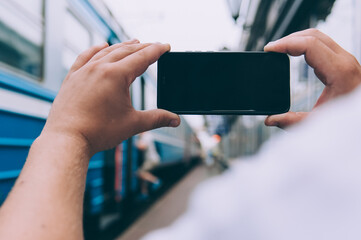 The guy holds a smartphone in his hands on the background of the train at the railway station.