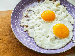 Close-up fried eggs in pink fryin pan on wooden board