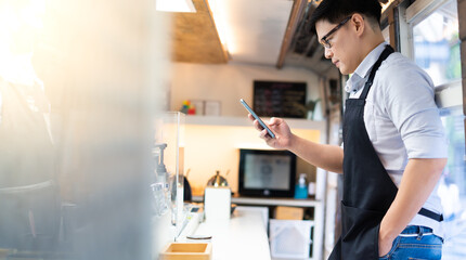 Portrait of confident Asian female barista standing inside bus coffee café. SME Business owner use smart phone for online marketing.