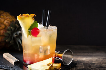 Cold mai tai cocktail with pineapple and cherry in glass on wooden table. Copy space	