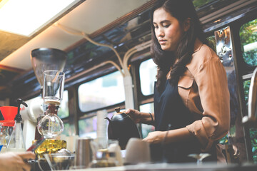Young Asian woman pouring milk into coffee making late coffee. Professional barista preparing coffee on counter