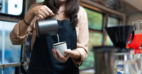 Young Asian woman pouring milk into coffee making late coffee. Professional barista preparing coffee on counter