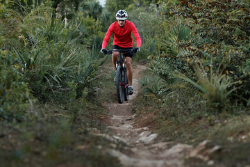 Front view of a cyclist riding narrow footpath, wearing bike helmet and red cycling jersey.