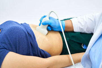 A person in a blue shirt, the girl is lying on the couch, she is given an ultrasound