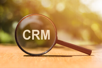 Magnifying glass with text CRM on wooden table.
