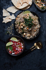 Indian rice and mushroom pilaf along with salad and popadum crackers on dark backround, copy space