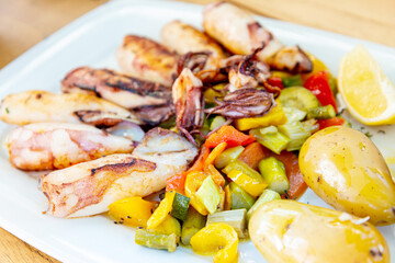 Delicious grilled whole squid with tomatoes, cucumbers slices, beetroots pieces and green dandelions served in white plate for an healthy mediterranean meal