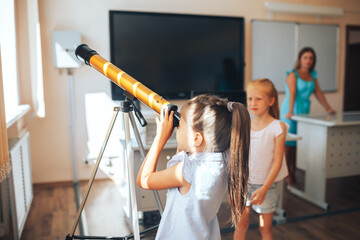 Two schoolgirls are looking through a telescope in an astronomy lesson, back to school, children's...