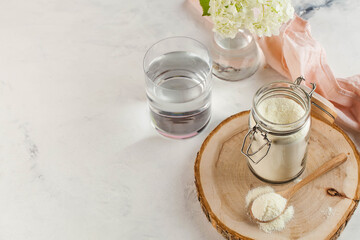 collagen powder in a wooden spoon, a glass of water, flower. Skin care, rejuvenation. Copy space.