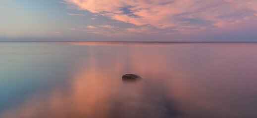 Open sea horizon at dawn. The sunlit clouds are reflected in the calm water of the Baltic Sea.
