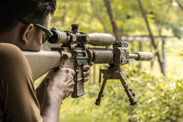 Military sniper with his precising sniper rifle aiming through scope and shooting in the shooting range 