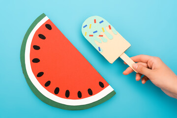 cropped view of woman holding paper ice cream with sprinkles near watermelon on blue background