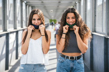 Portrait of a two young millennial friends lower the mask and smile -Tools need to wearing avoid...