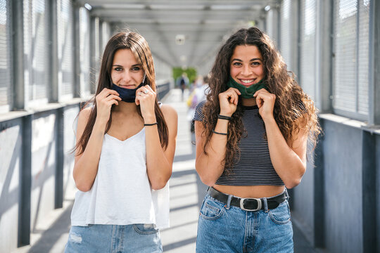 Portrait of a two young millennial friends lower the mask and smile -Tools need to wearing avoid the infection from Coronavirus, Covid-19 - People having fun together - Concept of freedom