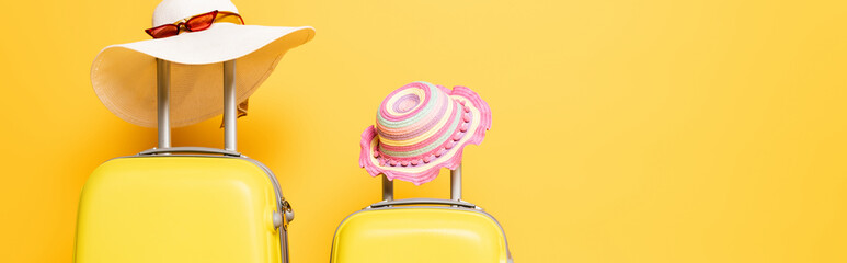 mother and daughter travel bags with sun hats and sunglasses isolated on yellow, panoramic shot