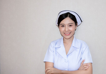 A gentle Asian young nurse in white clothing with arms folded isolated background. Portrait of smiley beautiful young nurse in white medical uniform holding hands crossed. Nurse or healthcare worker.