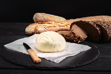 Loaf of bread with butter and knife. Dark background, side view