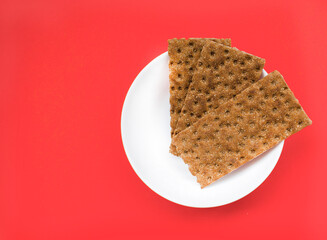 Healthy snack from wholegrain rye Crispbread Crackers on the red background. Top view. Rye crispbreads on colored background. Crispbreads on the bowl. Minimalism concept.
