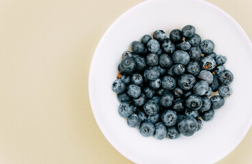 Blueberry in a white plate on a 
beige background. The composition of blueberry on a colored background. Healthy food. Minimalist food. Top view