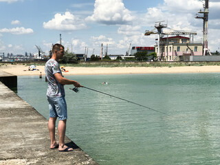 The guy is fishing on a spinning rod on the pier