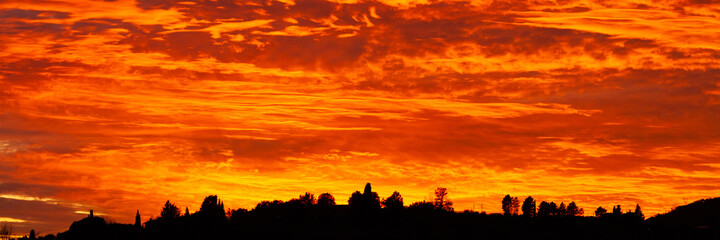 Obraz premium Beautiful sunset in Tuscany, Italy. Dramatic sky, bright red and orange colors, dark silhouettes of hills and trees. Banner